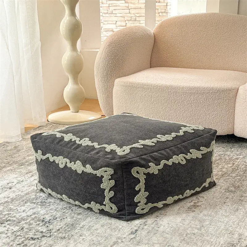 Pouf carré Sésame Nocturne en tissu brodé placé dans un salon moderne