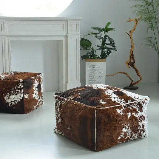Pouf carré imitation peau de vache utilisé comme décoration de salon