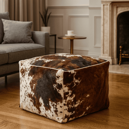 Pouf carré en fausse vachette dans un salon chic avec sol en bois, canapé gris et cheminée en pierre
